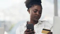 femme tenant une carte bancaire et un téléphone