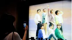 BTS의 광고판 앞에서 방탄소년단을 카메라에 담고 있는 팬 (본 기사와 무관함)