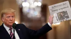 Trump akiwa ameshika gazeti lililoandika habari ya kusafishwa kwake
