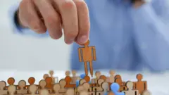 Mão levanta um boneco de papel de grupo com dezenas de figuras semelhantes