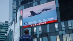 Man at shopping centre in Beijing watches a news broadcast showing a fighter jet during Chinese military operations near Taiwan, 3 August 2022