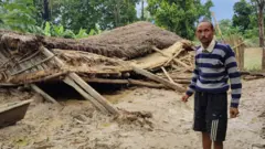 बाढीले भत्काएको घर अगाडि एकजना बाढीपीडित