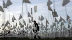 A man in a mask walks among flags representing those that died from Covid