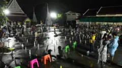 ประชาชนจำนวนมากไปต่อแถวเพื่อรอรับบัตรคิวเข้าตรวจเชิงรุกหาเชื้อโควิด-19 ท่ามกลางสายฝนที่ตกลงมาอย่างหนัก โดยแต่ละคนได้วางขวดน้ำและของใช้แทนตัวเองระหว่างหลบฝน ที่วัดบางขุนเทียนนอก เขตจอมทอง เมื่อ 9 ก.ค.