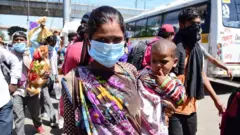 Una mujer migrante con un niño en sus brazos en la terminal de autobuses en Anand, India.
