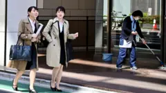 Women walk past a cleaner in Tokyo's Ginza district on April 3, 2019