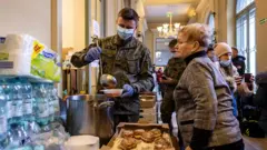Soldado serve sopa a uma ucraniana