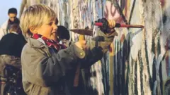 This photograph - taken on 12 November 1989 - shows a young boy chipping away at a section of the Berlin Wall, as the people in Berlin destroyed the wall that had divided their city for almost 30 years