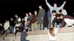 East German citizens climb the Berlin wall at the Brandenburg gate after the opening of the East German border was announced in Berlin on 9 November 1989