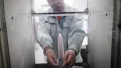 An employee of Japanese condom maker Sagami Rubber Industries puts a condom in a machine to test its endurance by filling it with air