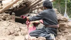 ভূমিকম্পে মাটির ঘরের ধ্বংস স্তূপ থেকে বিছানার অংশ বের করার চেষ্টা দেখা যাচ্ছে।