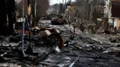 Soldiers walk past a destroyed Russian tank and armoured vehicles, amid Russia"s invasion on Ukraine in Bucha, in Kyiv region, Ukraine April 2, 2022.
