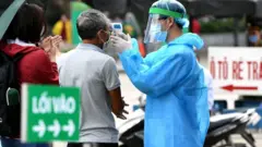 Nhân viên y tế mặc đồ bảo hộ kiểm tra nhiệt độ của người vào bệnh viện Bạch Mai, Hà Nội vào ngày 24 tháng 3 năm 2020