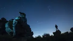 A plane passes by as a man stargazes at Brimham Rocks in Yorkshire as the Orionid meteor shower reaches its peak.