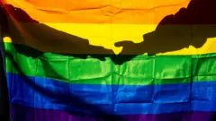 امرأتان تمسكان يدي بعضهما وأمامها علم قوس قزح