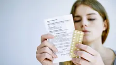 Une jeune femme lisant les instructions sur une notice de pilules