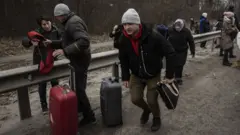 Fleeing civilians run with suitcases as they escape the town of Irpin, northwest of Kyiv, with blasts a few meters away on 6 March