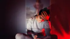 Mulher jovem olhando para o celular com expressão triste