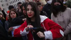 A young protester with red ink on her face that spells "HELP" cuts her hair with scissors during a demonstration against the death of Mahsa Amini on September 23, 2022 in Berlin, Germany