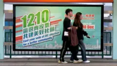 香港元朗某港鐵輕鐵站一對男女走過一幅政府宣傳區議會選舉的海報（BBC中文圖片19/11/2023）