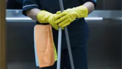 Mujer con guantes amarillos, toallas y una escoba