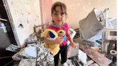 Tuta, la nieta de Samir con su peluche, en los restos de lo que fuera su casa.