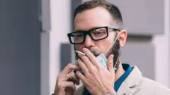 మాస్కు వేసుకుని పొగ తాగుతున్న వ్యక్తి