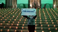 Em frente a escadaria com velas, manifestante segura cartaz que diz: 'Onde erramos?'