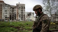 A Ukrainian serviceman walks near a residential building damaged by shelling in the frontline city of Bakhmut