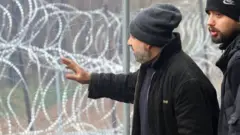 Migrants stand next to a razorwire fence on the Belarus-Poland border