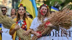 فتاتان تحملان أغصان القمح المغطاة بالطلاء الأحمر أثناء مسيرة في وسط أثينا خلال مسيرة لدعم أوكرانيا في 31 يوليو/ تموز 2022