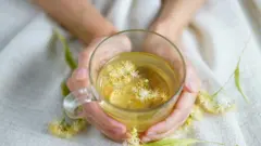 Mujer sosteniendo taza de té de flores en cama