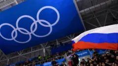 A Russian flag is waved in front of the Olympic rings at Pyeongchang 2018