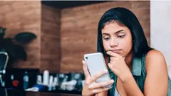 Una mujer mria con cara de preocupación su teléfono celular.
