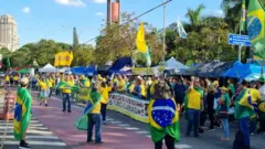 Pessoas vestindo amarelo em pé, com barracas ao fundo