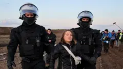 Greta Thunberg held by police officers at climate protest