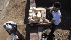 Homem com máscara e protetor visual distribui comida para população em situação de necessidade