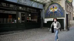 A woman in a mask walks past a closed restaurant in Brussels