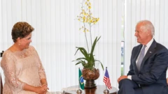 Dilma e Biden sorriem um para o outro, sentados em sala