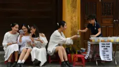 A woman serves food to a group of young women, sitting outdoors