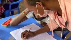 Umukobwa ariko arandika mw'ikaye n'ikiramu y'igiti(crayon)