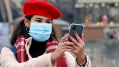 A woman wearing a protective face mask takes a selfie in front of the Eiffel Tower in December