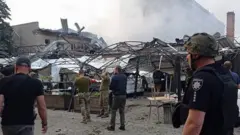 Ukrainian rescuers and policemen work on the site of a rocket hit in downtown Kramatorsk