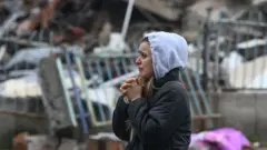 भत्किएको भवन हेर्दै एक महिला