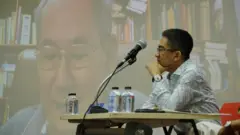 วรเจตน์ ภาคีรัตน์ นั่งอยู่หน้าจอที่มีภาพนิธิ เอียวศรีวงศ์