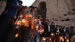 People holding lanterns stand beside the cliff