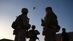 US Marines and Afghan Commandos stand together as an Afghan Air Force helicopter flies past during a combat training exercise at Shorab Military Camp in Lashkar Gah in Helmand province, on 27 August 2017.