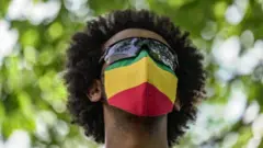 ናይ ኢትዮጵያ ባንዴራ ዘለዎ መሸፈኒ ኣፍን ኣፍንጫን ዝገበረ ሰብኣይ