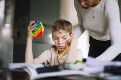 Mãe ajuda filho com lição de casa enquanto ele mexe em brinquedo