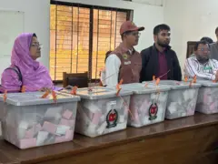 পাঁচটি ব্যালট বাক্স নিয়ে দাঁড়িয়ে আছেন চারজন